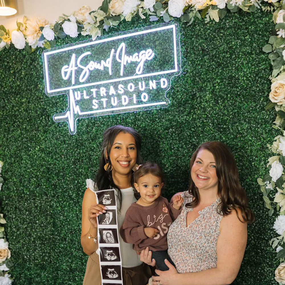 women holding a baby and ultrasound result with neon sign on wall