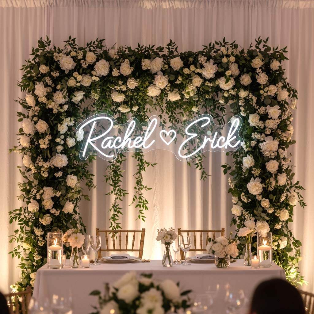 Custom white neon couple-name sign surrounded by flowers at a wedding reception