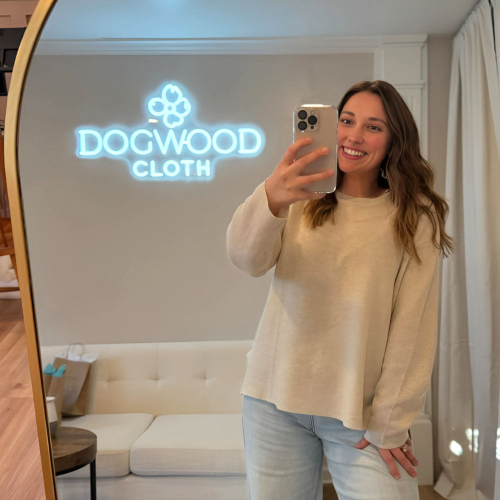 Dogwood Cloth Owner taking a mirror selfie in a room with a 'Dogwood Cloth' neon sign.